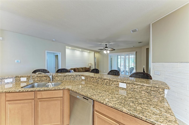 kitchen featuring stainless steel dishwasher, a sink, open floor plan, light stone counters, and a ceiling fan