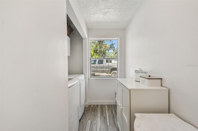 clothes washing area with light wood finished floors, cabinet space, a textured ceiling, baseboards, and independent washer and dryer