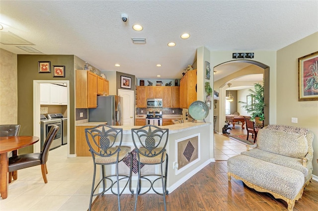 4211 30th Ln E, Bradenton, FL 34208 - kitchen with washing machine and dryer, visible vents, arched walkways, light countertops, and appliances with stainless steel finishes