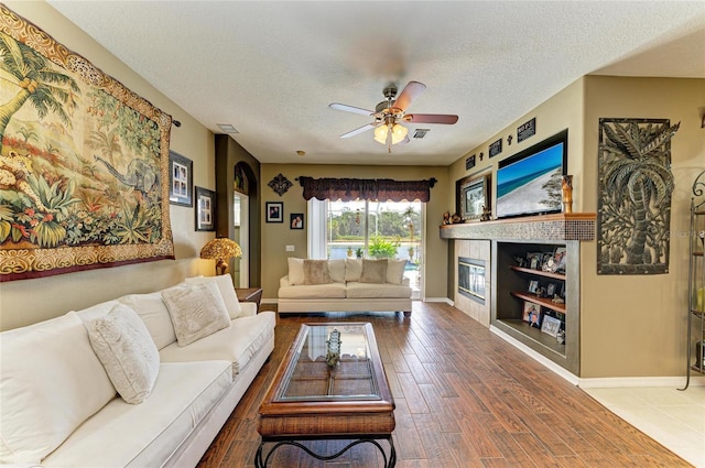 4211 30th Ln E, Bradenton, FL 34208 - living room featuring wood finished floors, a textured ceiling, ceiling fan, baseboards, and a glass covered fireplace