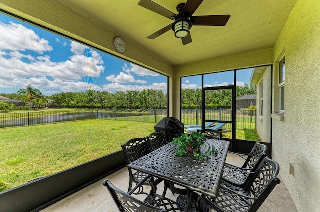 sunroom with a water view, a ceiling fan, outdoor dining space, and view of wooded area