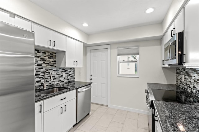 kitchen featuring a sink, dark stone countertops, white cabinetry, baseboards, and appliances with stainless steel finishes