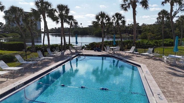 pool with a patio area, a water view, and fence