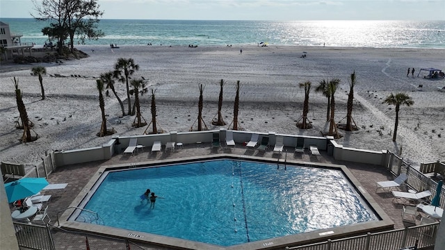 pool with a water view, a patio area, and a view of the beach