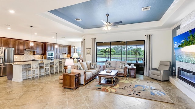 20359 Cristoforo Pl, Venice, FL 34293 - living area featuring a tray ceiling, ornamental molding, ceiling fan, and a fireplace