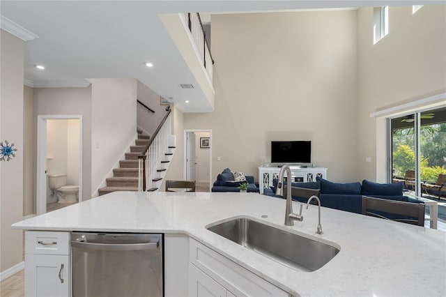 kitchen with white cabinetry, stainless steel dishwasher, open floor plan, and a sink