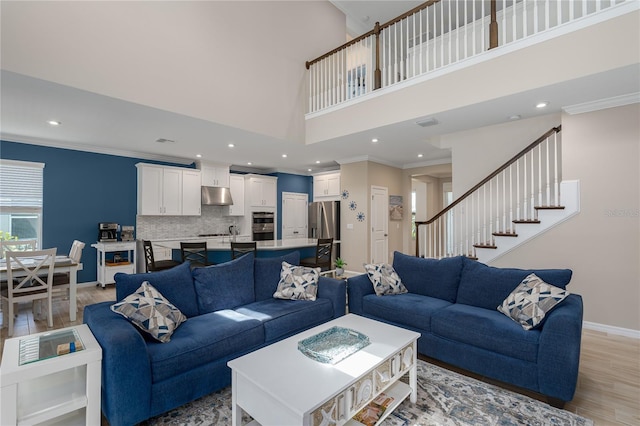 living room with a high ceiling, light wood-type flooring, baseboards, ornamental molding, and recessed lighting