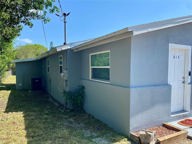 view of side of property with a lawn, central AC unit, and stucco siding
