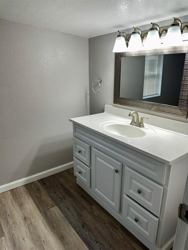 bathroom featuring wood finished floors, a textured ceiling, baseboards, a textured wall, and vanity