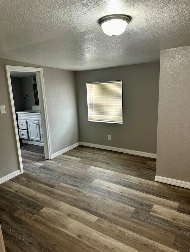 empty room featuring a textured ceiling, a textured wall, baseboards, and wood finished floors