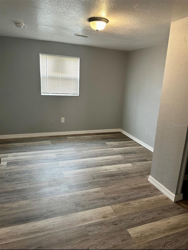 spare room featuring baseboards, visible vents, a textured ceiling, and wood finished floors
