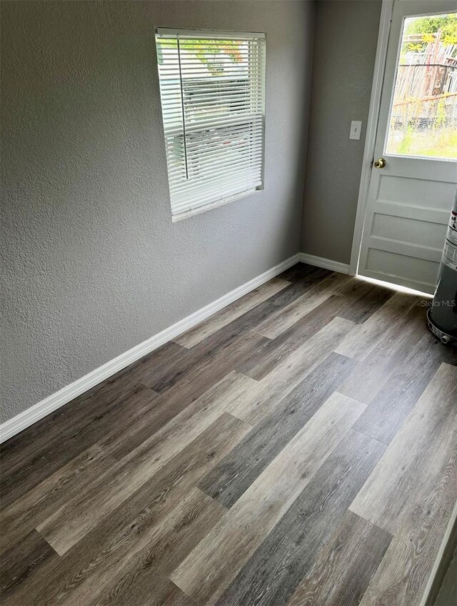empty room featuring a textured wall, baseboards, dark wood-style floors, and plenty of natural light