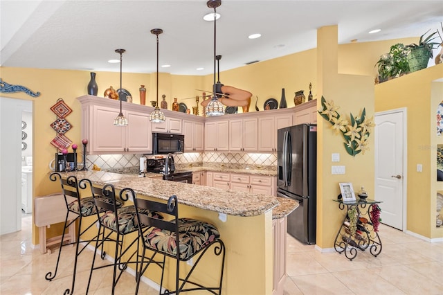 490 Pine Lily Way, Venice, FL 34293 - kitchen with black appliances, a peninsula, a kitchen breakfast bar, tasteful backsplash, and light stone countertops