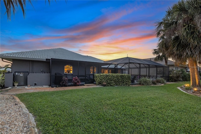 490 Pine Lily Way, Venice, FL 34293 - back of house at dusk featuring a lawn, a tile roof, glass enclosure, and stucco siding