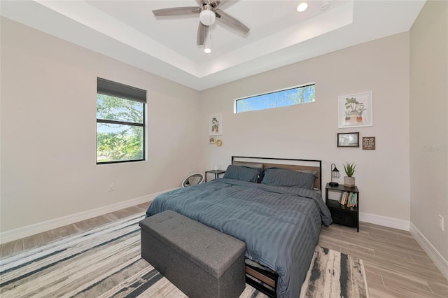 bedroom with light wood finished floors, a raised ceiling, baseboards, recessed lighting, and a ceiling fan