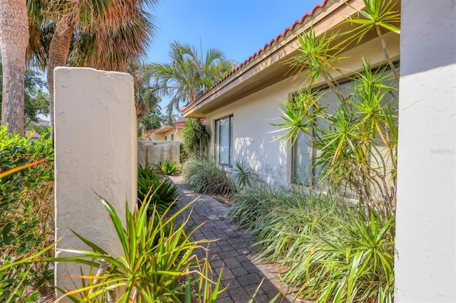 view of side of home with a tiled roof, stucco siding, and fence
