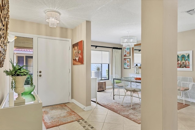 entrance foyer featuring a chandelier, light tile patterned flooring, baseboards, and a textured ceiling