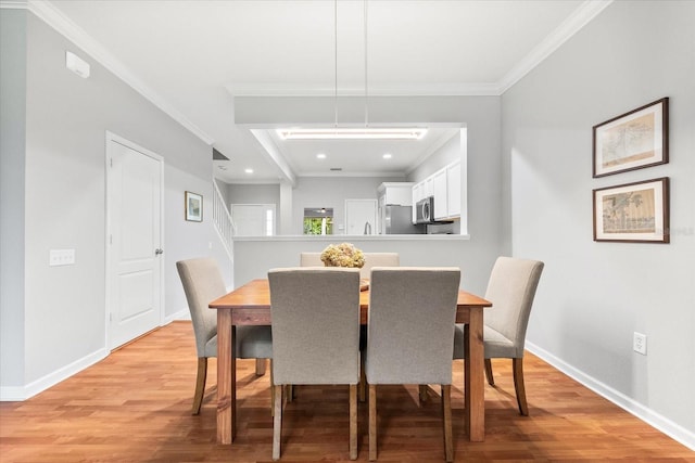 dining room featuring light wood finished floors, crown molding, baseboards, recessed lighting, and stairway