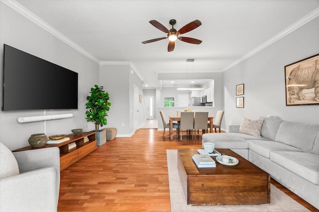living room with ornamental molding, light wood-style flooring, a ceiling fan, and baseboards