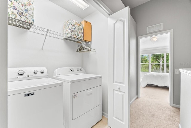 clothes washing area featuring washer and clothes dryer, light colored carpet, and baseboards