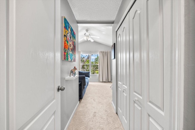 corridor with carpet floors, a textured ceiling, lofted ceiling, and baseboards
