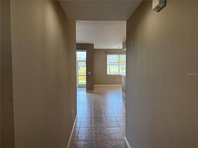 corridor featuring a textured ceiling, a chandelier, baseboards, and light tile patterned flooring