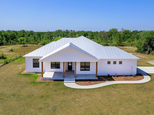 view of front facade featuring a porch, a wooded view, metal roof, and a front lawn