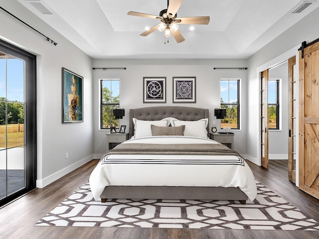 bedroom featuring a tray ceiling, visible vents, a barn door, and access to exterior