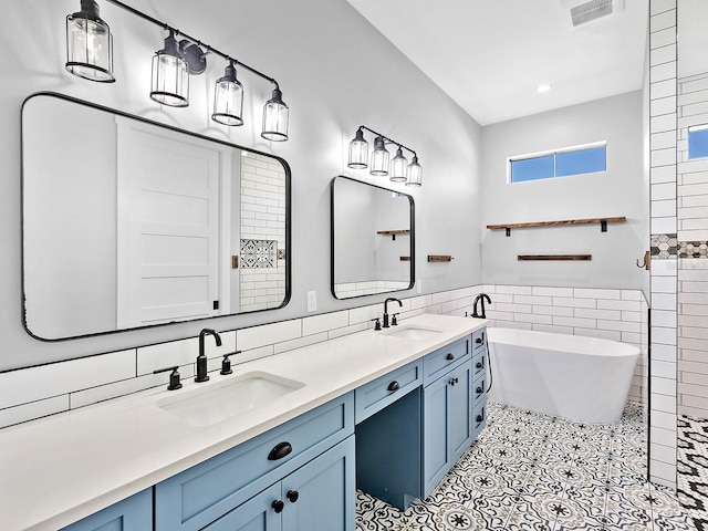 bathroom with tile walls, a freestanding tub, visible vents, and a sink