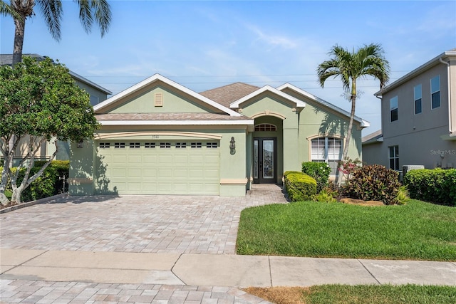 view of front of house with stucco siding, an attached garage, decorative driveway, a front lawn, and roof with shingles