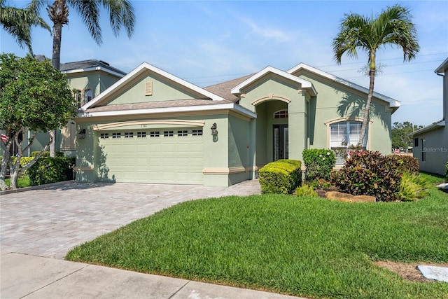 ranch-style home featuring stucco siding, a garage, decorative driveway, and a front lawn