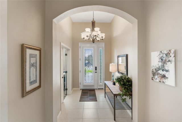 foyer featuring baseboards, arched walkways, a chandelier, and light tile patterned floors