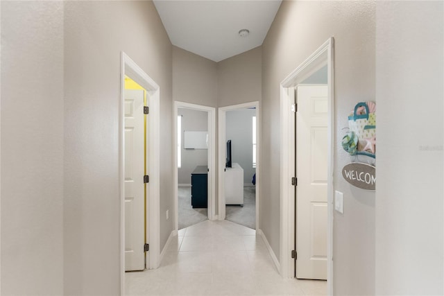 hallway with light tile patterned floors, baseboards, and light colored carpet