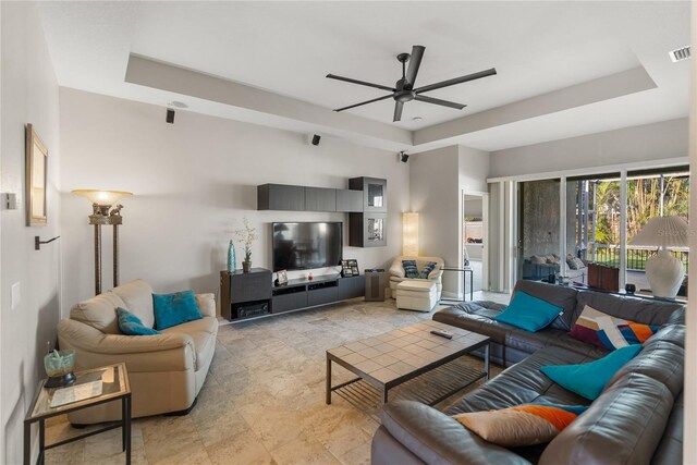 living area with ceiling fan and a tray ceiling