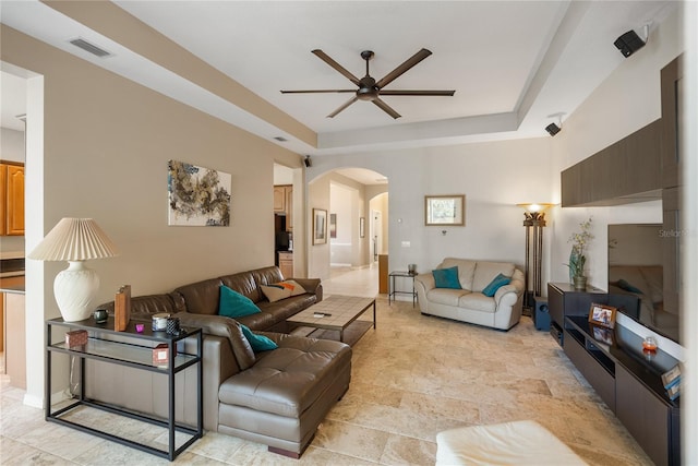 living area featuring a ceiling fan, arched walkways, and a raised ceiling