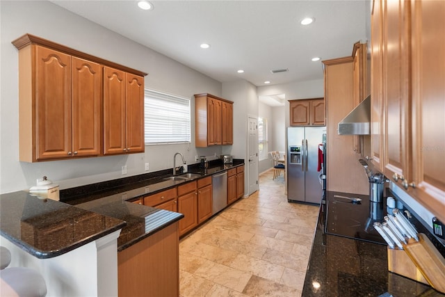 kitchen with stainless steel appliances, a sink, a peninsula, ventilation hood, and dark stone countertops
