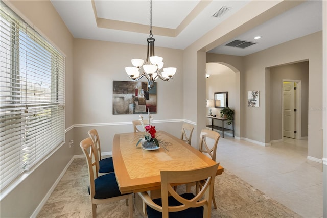 dining space featuring arched walkways, a chandelier, baseboards, a raised ceiling, and light tile patterned floors