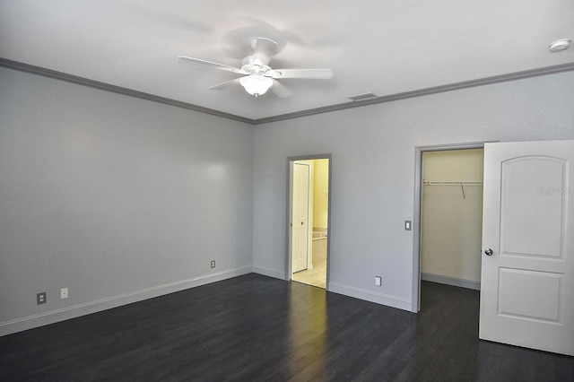 unfurnished bedroom featuring crown molding, dark wood-style flooring, a spacious closet, and baseboards