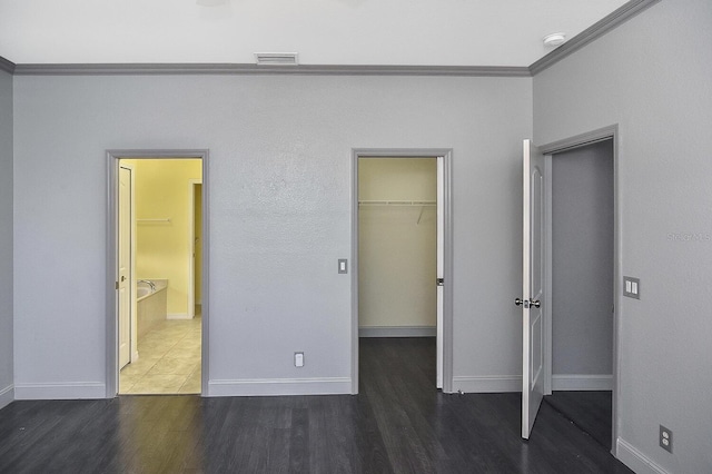 unfurnished bedroom with wood finished floors, visible vents, crown molding, a walk in closet, and baseboards