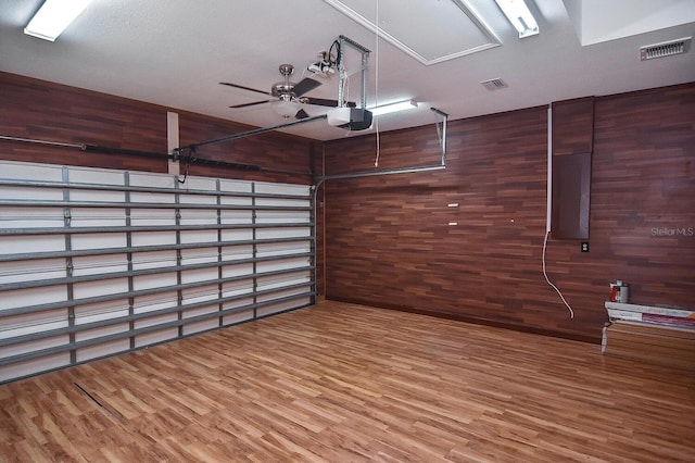 garage featuring a ceiling fan, wooden walls, a garage door opener, and visible vents