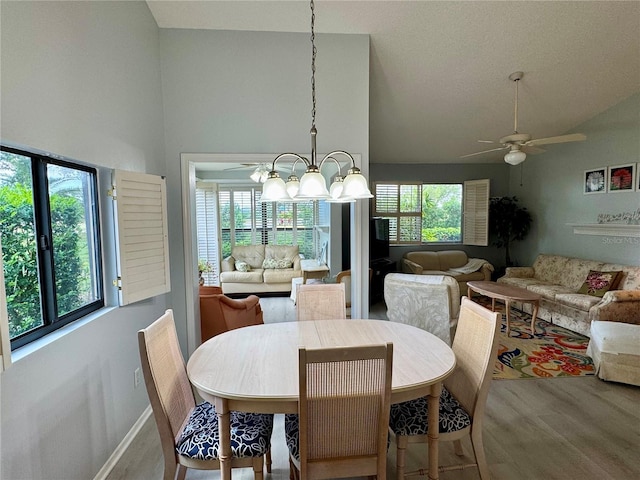 dining area featuring wood finished floors, a ceiling fan, a chandelier, baseboards, and high vaulted ceiling