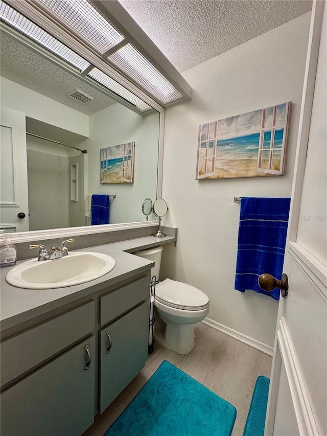 bathroom featuring wood finished floors, toilet, vanity, a textured ceiling, and baseboards