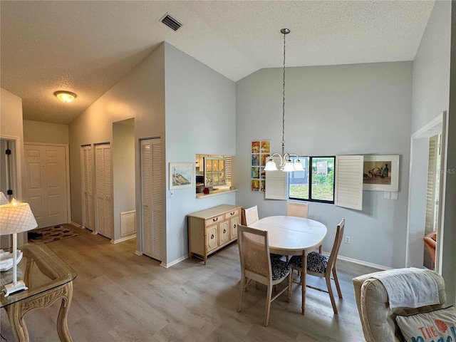 dining space featuring light wood-style flooring, a textured ceiling, baseboards, an inviting chandelier, and visible vents