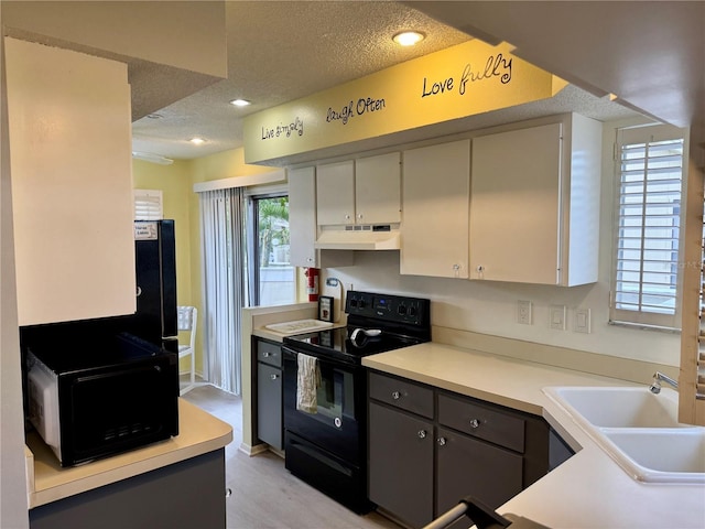 kitchen featuring black appliances, a textured ceiling, a sink, under cabinet range hood, and light countertops