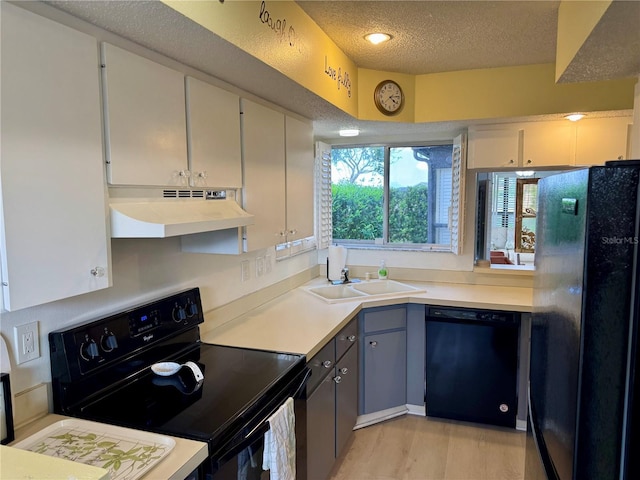 kitchen featuring black appliances, under cabinet range hood, a sink, light wood finished floors, and light countertops