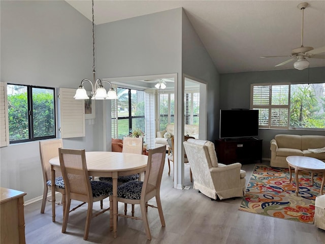 dining space featuring a ceiling fan, light wood-type flooring, high vaulted ceiling, a chandelier, and baseboards