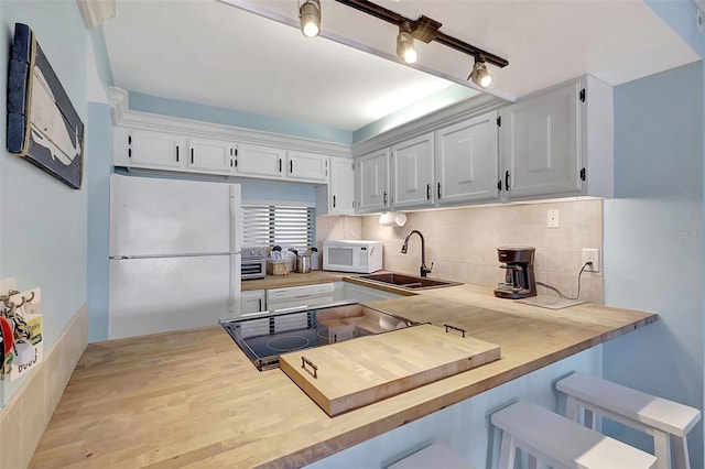 kitchen with white appliances, wooden counters, a sink, decorative backsplash, and white cabinets