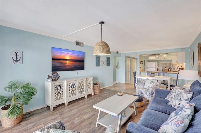 living room featuring light wood-type flooring, visible vents, baseboards, and ornamental molding