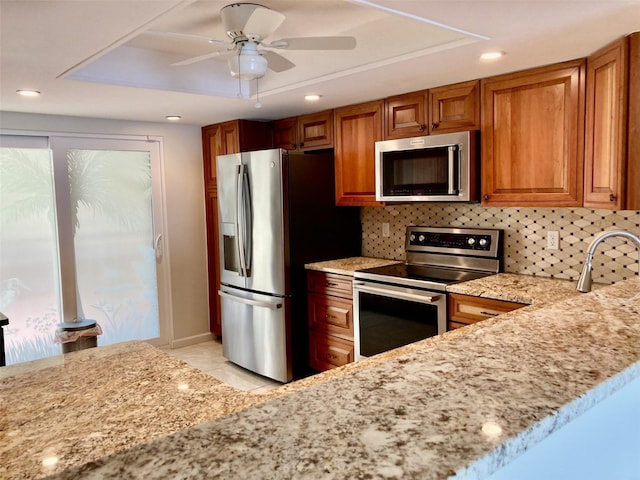6430 Sun Eagle Ln Unit 203, Bradenton, FL 34210 - kitchen with appliances with stainless steel finishes, light stone countertops, brown cabinetry, a ceiling fan, and decorative backsplash