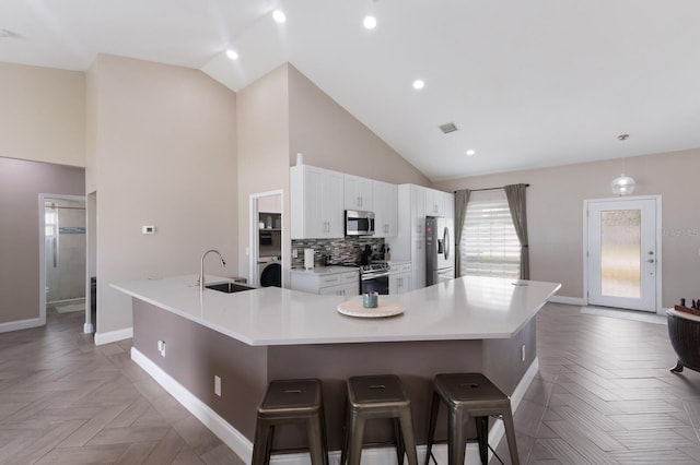 kitchen featuring appliances with stainless steel finishes, baseboards, a sink, light countertops, and a kitchen breakfast bar